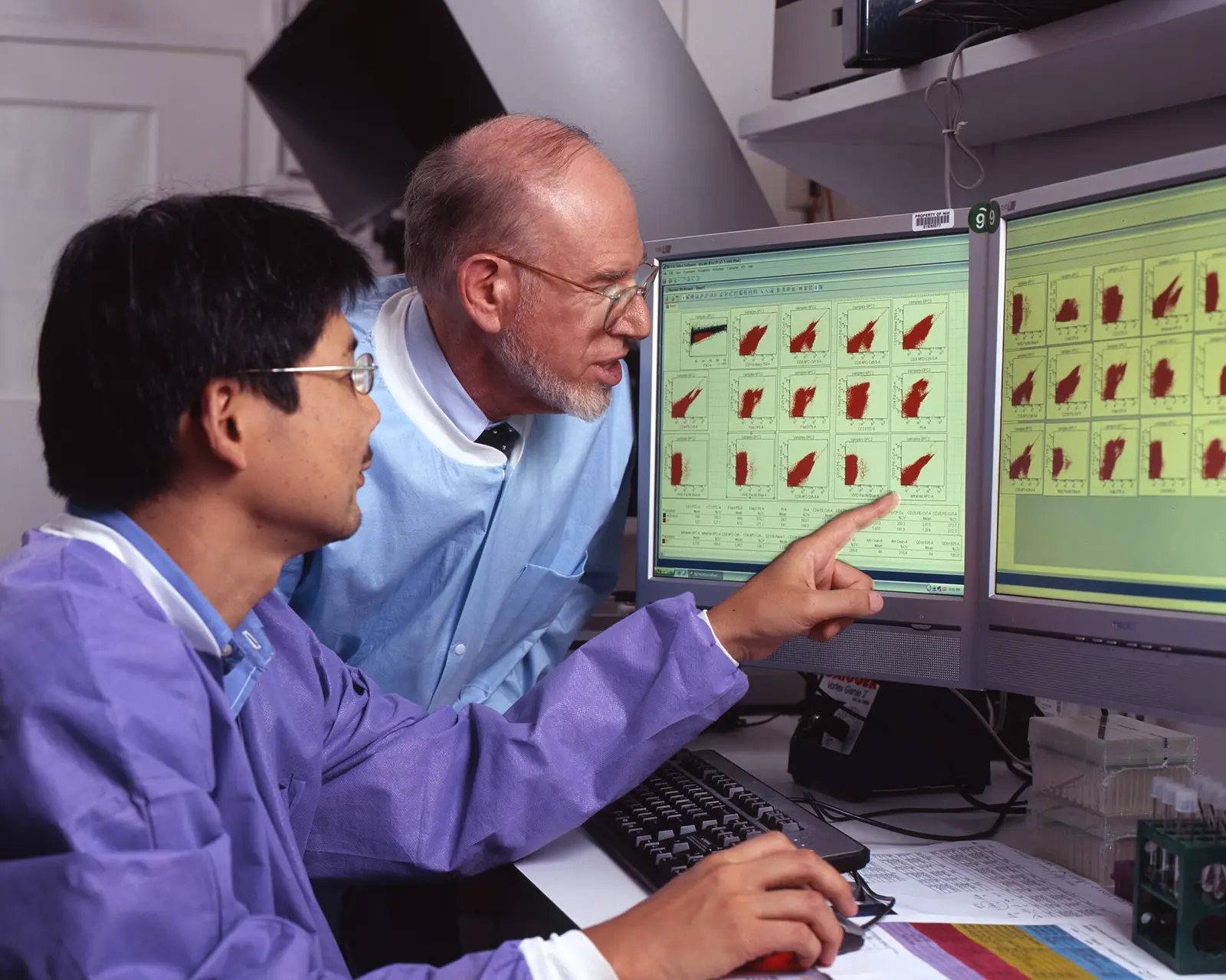 Two cancer researchers reviewing experimental data together on laboratory monitors